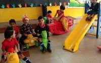 Kindergarten children in an indoor play area with a slide and ride-on toys